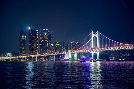 广安桥摄影照片_光岸大桥和摩天大楼在夜色中灯火通明。韩国釜山。光岸大桥和夜间的摩天大楼。韩国釜山
