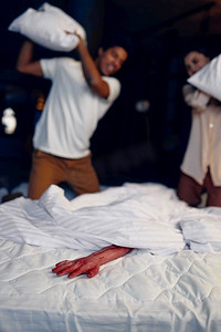 血淋淋的摄影照片_一对惊恐的家庭夫妇在床上用枕头袭击了血淋淋的幽灵手。选择性聚焦。夫妇在床上用枕头袭击血淋淋的手