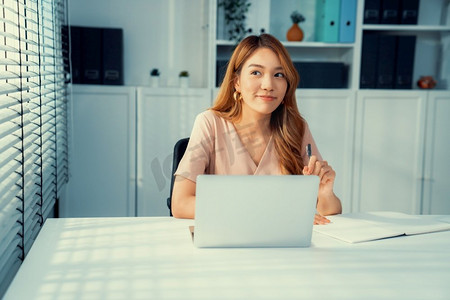一位年轻的亚洲女性坐在她办公室的办公桌前.