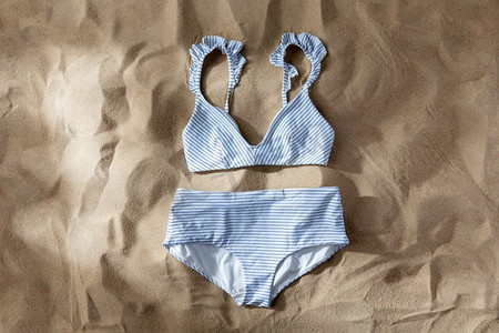 泳装摄影照片_时尚，泳装和暑假概念-海滩沙滩上和底部的条纹白色蓝色泳衣。沙滩上的白色蓝色条纹泳衣