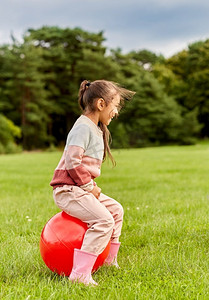 童年，休闲和人的概念—快乐的小女孩跳在公园。快乐的小女孩弹跳在hopper球在公园