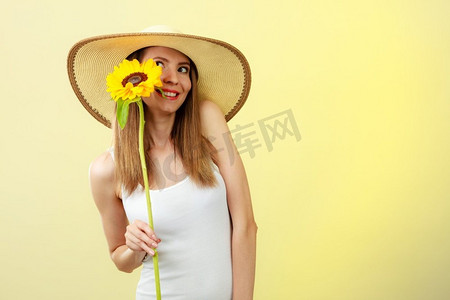 戴花的美女摄影照片_黄色背景下手持向日葵、头戴草帽的夏日美女特写