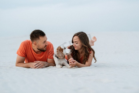 沙滩衣服摄影照片_年轻夫妇橙色衣服与狗在沙漠白色的沙滩