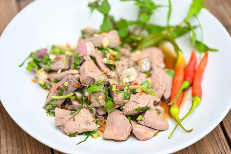 薄荷背景摄影照片_辛辣的肝沙拉在白色板木桌子背景，与新鲜的辣椒香草，香料，泰国食物的猪肝沙拉 
