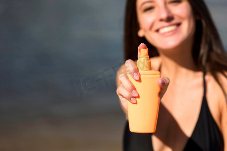 微笑的女人拿着防晒霜海滩，带文案空间