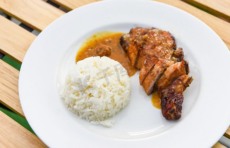 泰国饭食物，熟的白米饭和烤鸡有酱汁在白色盘子和木桌子背景，辛辣的烧烤鸡腿