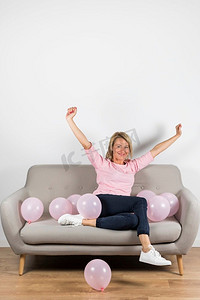 兴奋的成熟金发女郎女人坐沙发与粉红色气球提高她的手臂