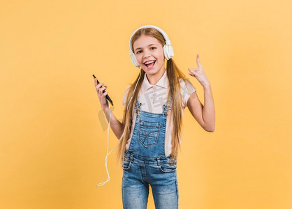 快乐的女孩听音乐耳机做摇滚标志反对黄色背景