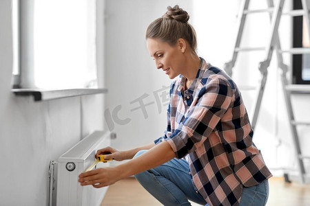 维修，改善和翻新概念—妇女与尺子测量加热器在家里。妇女与尺子测量加热器在家里
