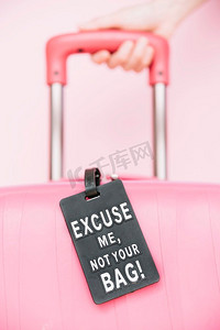 人的手握手柄旅行箱与您的袋标签反对粉红色背景