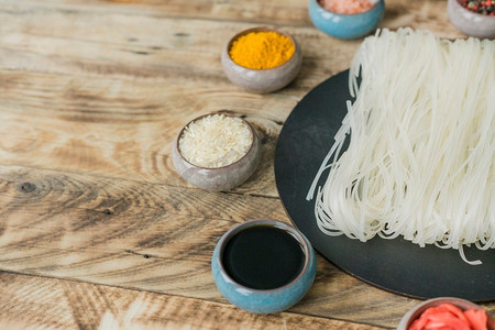 酱油生米姜黄碗附近的干米粉黑色托盘木纹理背景