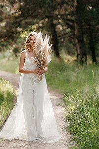 森林小路上，穿着白色轻裙，手捧一束干花的快乐新娘女孩