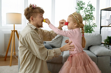 爸爸和女儿戴着小丑鼻子在一起玩，幸福的全家福。爸爸和女儿穿着小丑鼻子玩得开心