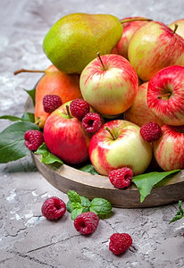 具体背景摄影照片_新鲜的乌藨子和苹果在一个具体背景的老木盘子。健康的概念。天然健康食品有机食品。