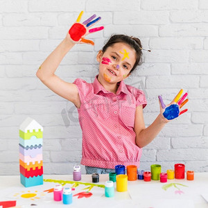 可爱的小女孩展示画的手站在前面的桌子与五颜六色的颜色