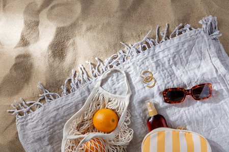 休闲和暑假概念-沙滩毛毯上的橙子和防晒油袋子。沙滩毛毯上的一袋橙子和防晒油