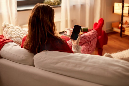 圣诞节，冬季假期和休闲概念—年轻妇女使用智能手机在舒适的家。妇女使用智能手机在家里圣诞节
