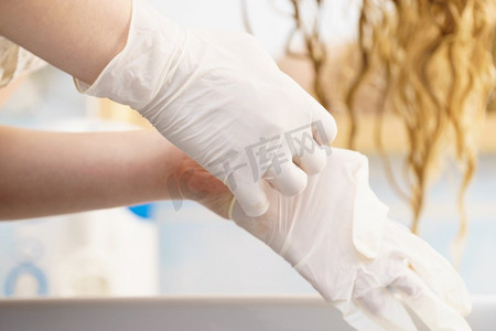 妇女在浴室里穿上白色乳胶保护手套之前头发染色。妇女与白色乳胶手套在浴室