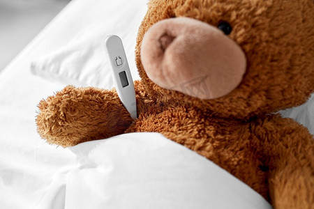 医学，保健和儿童概念—生病的泰迪熊玩具头与温度计躺在床上。生病的泰迪熊玩具头与温度计在床上