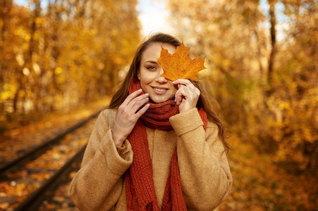 美丽的快乐的微笑的妇女的秋天肖像覆盖眼睛与金叶子在橙色秋天叶子。肖像的妇女覆盖眼睛与叶