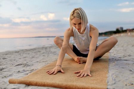 健身，运动，和健康的生活方式概念—妇女做瑜伽伸展姿势在海滩超过日落。妇女做瑜伽伸展姿势在海滩