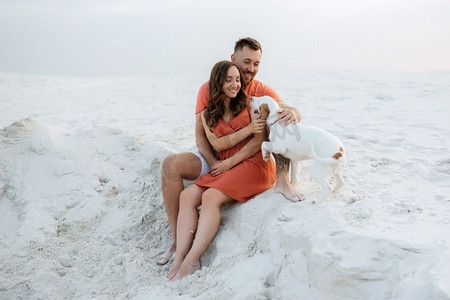 年轻夫妇橙色衣服与狗在沙漠白色的沙滩