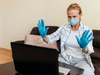 隔离期间戴着医用口罩的妇女在家中工作笔记本电脑