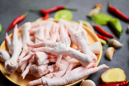 生鸡摄影照片_新鲜的生鸡爪放在厨房的木桌上做熟食，鸡爪放在盘子里