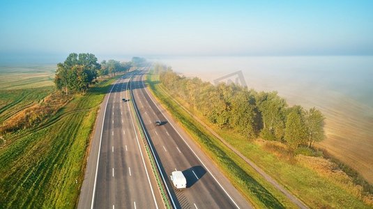 光魔法摄影照片_阳光明媚的魔法秋天雾的早晨。鸟瞰高速公路与汽车。沥青路被雾覆盖。清晨的薄雾。白俄罗斯M1 Alumstaral