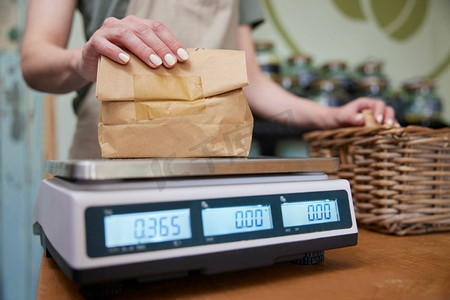 关闭销售助理在可持续的塑料免费杂货店称重货物在纸袋在数字秤