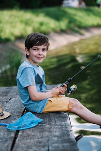 快乐的男孩坐在木质码头湖上，手里拿着钓竿