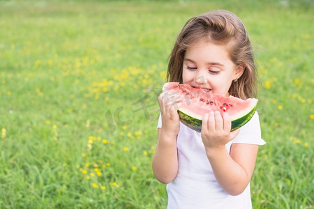 小女孩站在田野吃红片西瓜