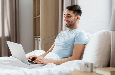 人，技术和远程工作概念—人与笔记本电脑躺在床上在家庭卧室。男人与笔记本电脑在床上在家庭卧室