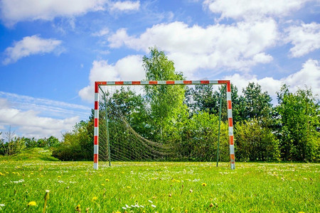 旧手球目标与一个破碎的网在绿色草坪在夏天与蓝天