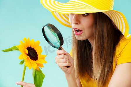 植物学家摄影照片_植物学家妇女惊讶的脸表情在黄色帽子审查通过放大镜看花在蓝色背景