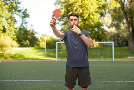 体育,足球和裁判概念 — 男裁判吹口哨,在足球场背景上出示红色罚单.