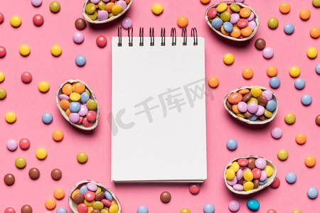 空白螺旋记事本包围着五颜六色的宝石糖果粉红色背景