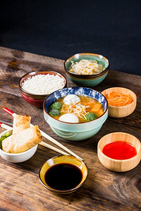 米春卷酱汁豆芽磨碎的胡萝卜与鱼丸汤桌子反对黑色背景