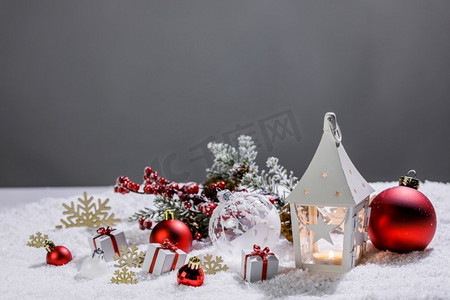 小玩意儿摄影照片_圣诞装饰与蜡烛在灯笼小玩意儿和礼物在雪。圣诞装饰灯笼