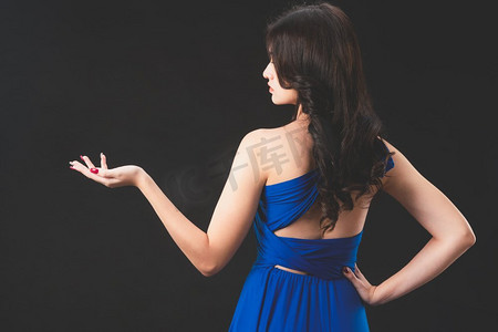 站在黑暗背景的蓝色礼服美丽的妇女时尚模特。奢侈品广告。