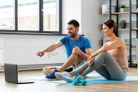 健身，运动和技术概念—快乐夫妇与笔记本电脑做运动在家里。快乐的夫妇与笔记本电脑做体育在家里