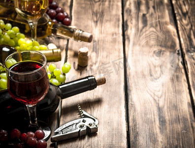 葡萄和红酒杯摄影照片_带有白葡萄和红葡萄枝条的玻璃杯红葡萄酒。在一张木桌上..新鲜红葡萄酒和白葡萄酒