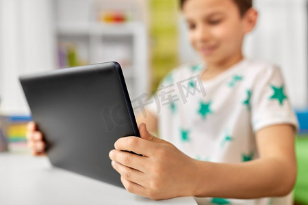 童年、科技和人的概念--男孩坐在桌子旁的平板电脑特写。男孩和平板电脑坐在桌子旁的特写