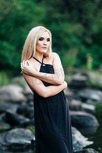 金发女孩在一件黑色的裙子与蓝色的眼睛在河的石头海岸
