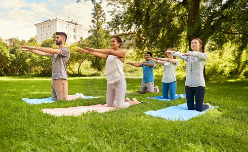 健身、运动和健康生活方式的概念-一群快乐的人在夏季公园做瑜伽。一群人在夏季公园做瑜伽