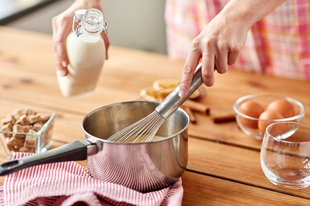 打假日摄影照片_烹饪，烹饪和季节性饮料的概念—近距离的手与搅拌器和牛奶使蛋酒在锅。手用打蛋器和牛奶煮蛋酒