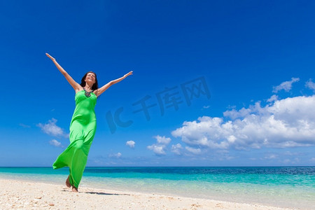 绿色衣服的妇女摆在热带海滩有提出的手臂摆在蓝天背景。女人在绿色的衣服在海滩