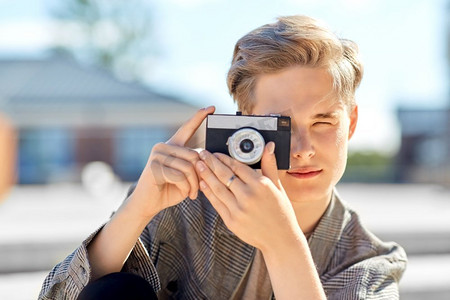 休闲、科技和人的概念--城市中的年轻人或十几岁的男孩拿着相机拍摄。拿着相机在城市里拍照的年轻人