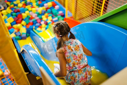 小女孩骑在塑料儿童滑梯，游乐场在娱乐中心。室内游戏区，游戏室