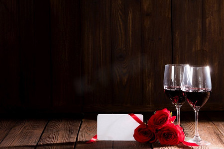 两杯红酒,红玫瑰和空白贺卡在深色木制背景浪漫约会情人节酒杯地板